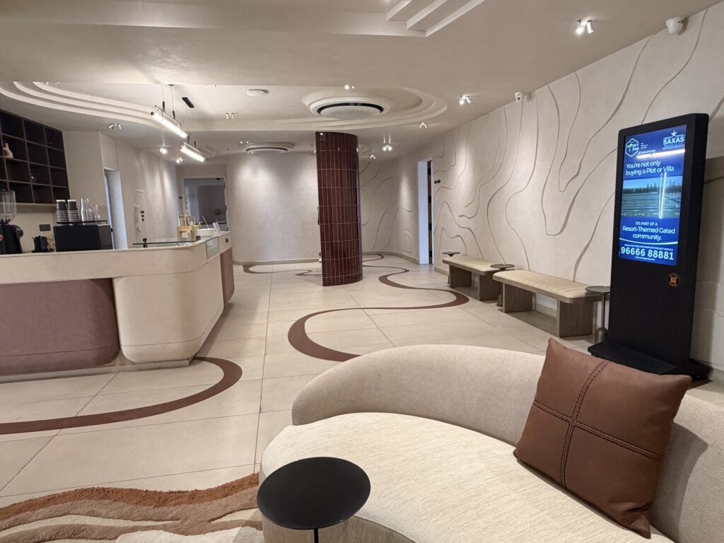 Freestanding digital advertising screen beside curved lounge seating and a reception counter at Kor Klub.