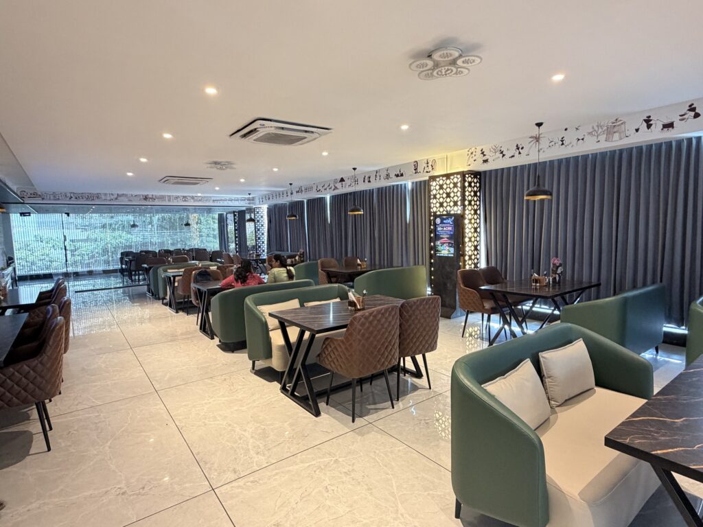 Digital advertising screen between dining tables and green upholstered seating at Avuna Restaurant.