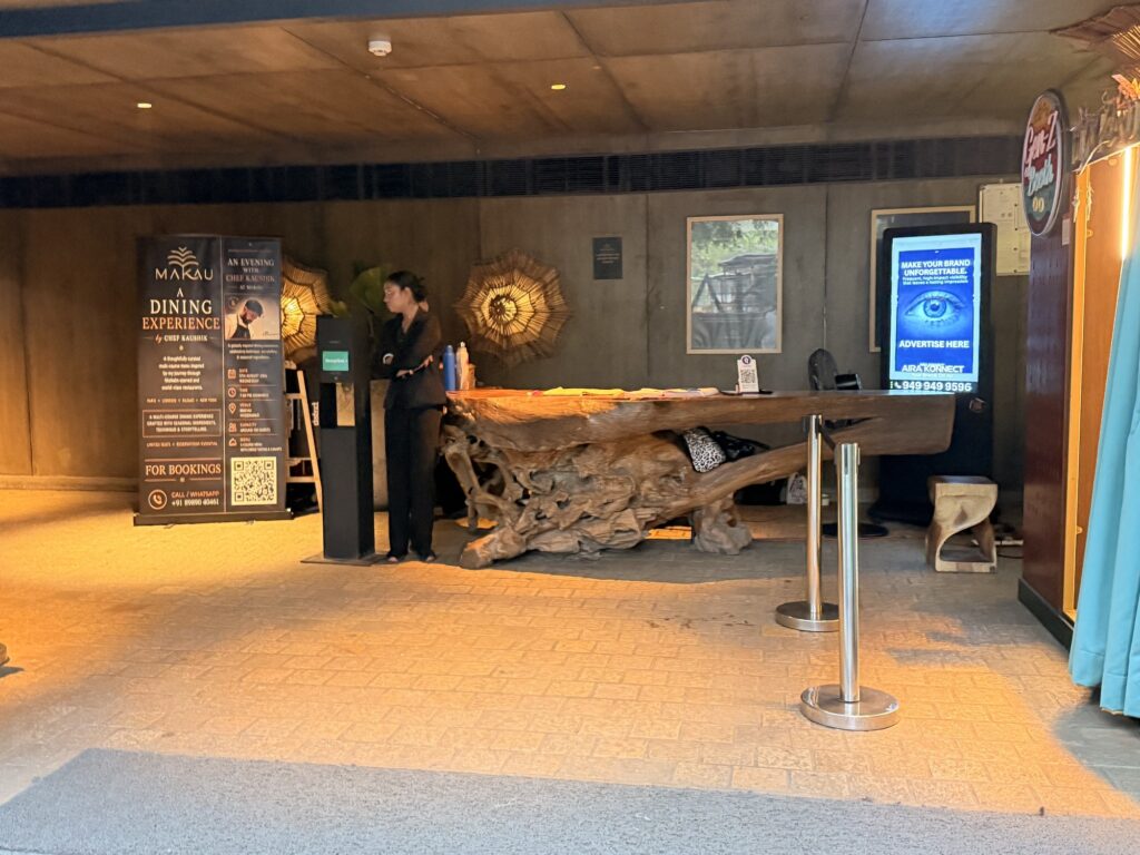 Digital advertising screen behind a sculptural wooden reception desk at Makau.