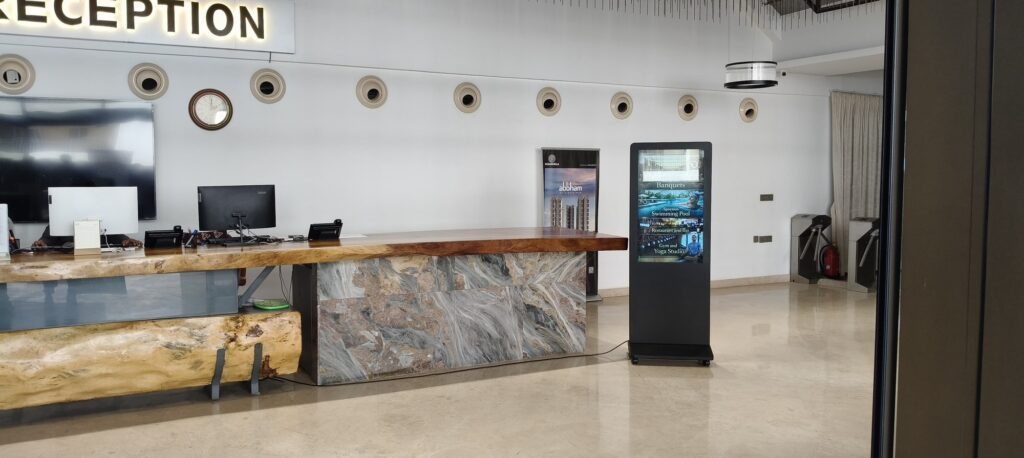 Freestanding digital advertising screen beside a marble reception counter at TCCC Kondapur.